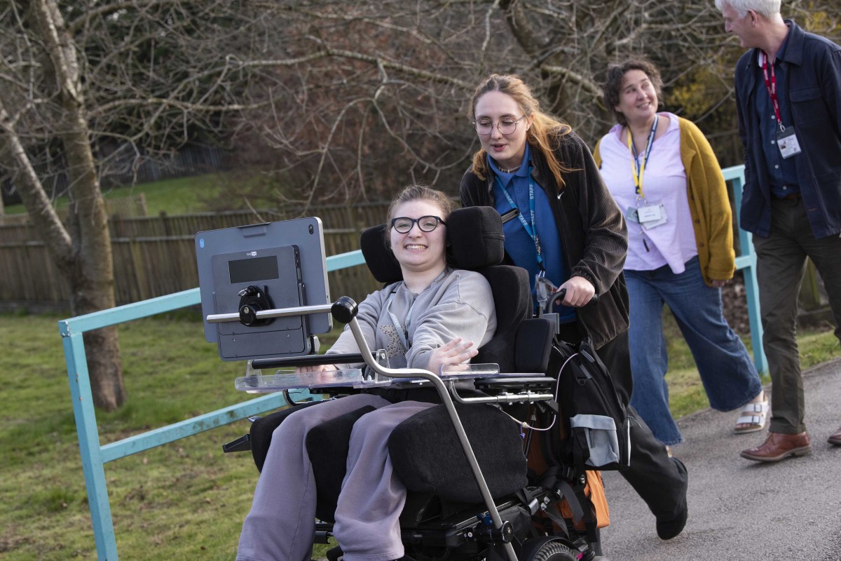 Milly out in the park with her Grid Pad mounted to her chair, looking happy to have it with her.