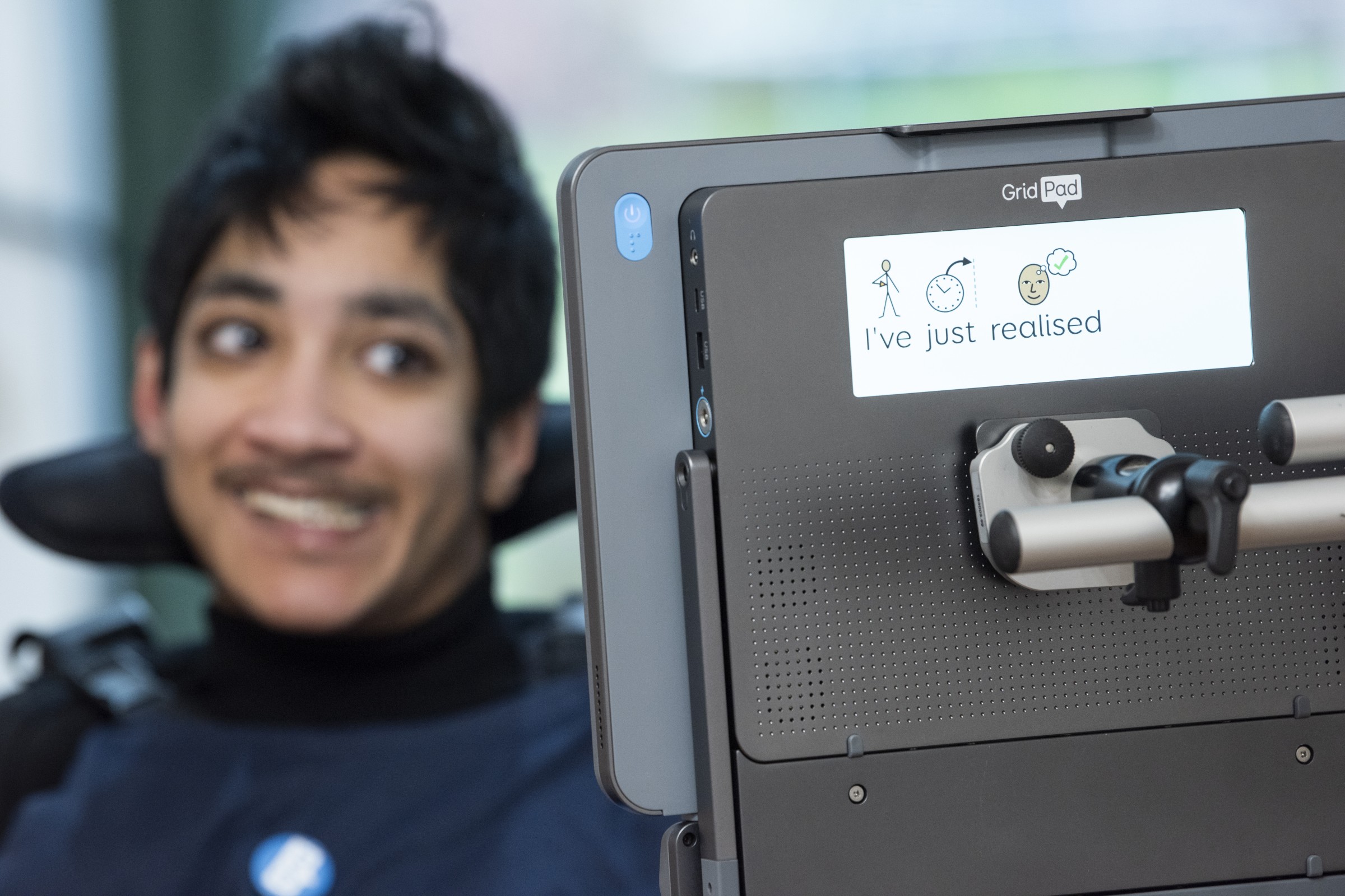 A young man smiling while looking at a Grid Pad 13 device. You can see the second screen showing a message that reads 'I've just realised' with text and symbols.