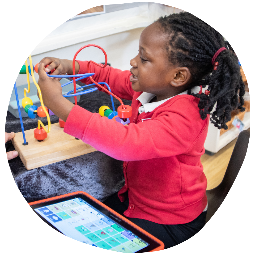 child playing with a bead maze with an iPad with Grid software on it next to her