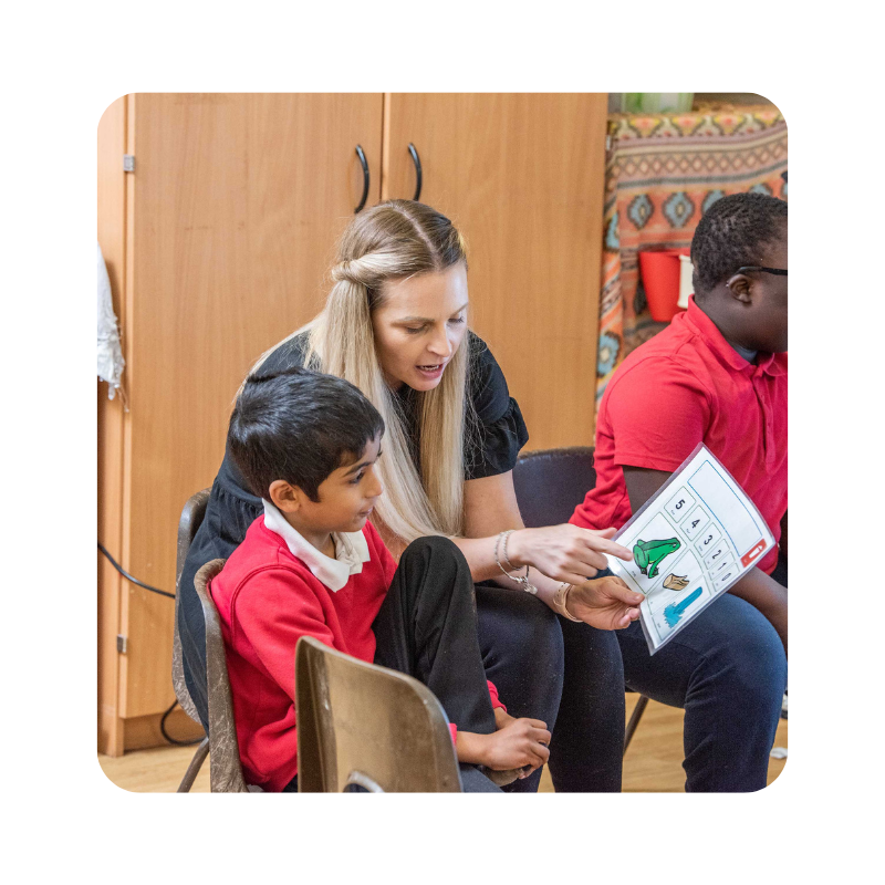 Teacher and student looking at a low tech AAC resource, with an image of a frog, a log and a waterfall.