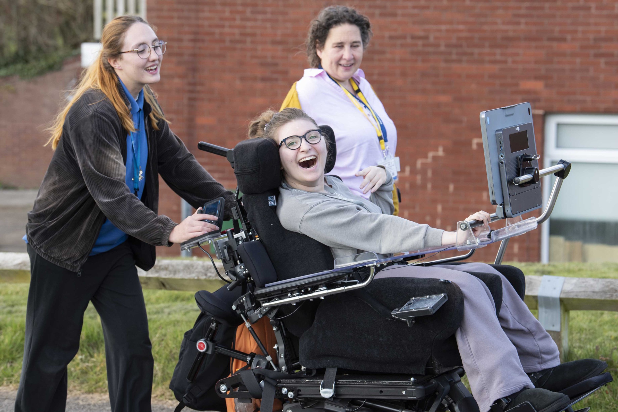 Milly, Saffron (AAC specialist), and another girl in the park, all happy. Milly’s using the Grid Pad 16 outdoors, enjoying the daylight-bright display and anti-glare coating.
